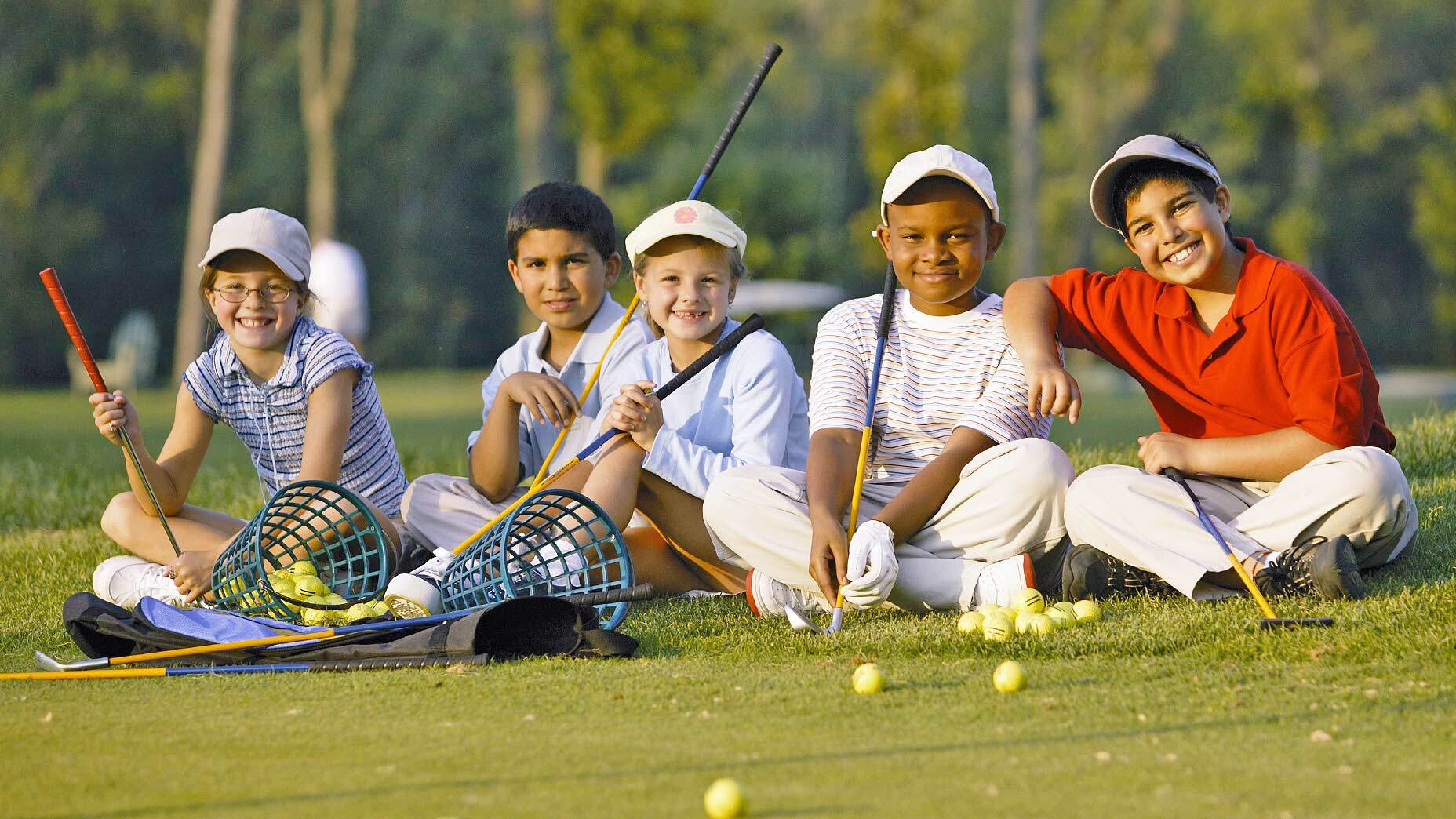 An image of children with golf clubs sitting on a golf course. 